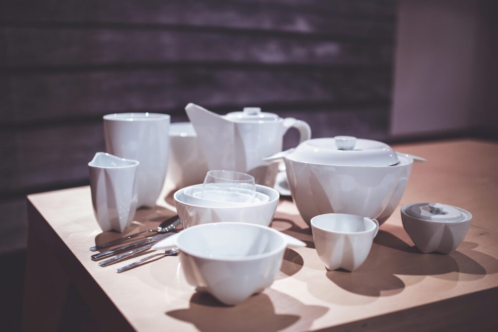 A stylish arrangement of white porcelain tableware including cups, bowls, and cutlery on a wooden table.